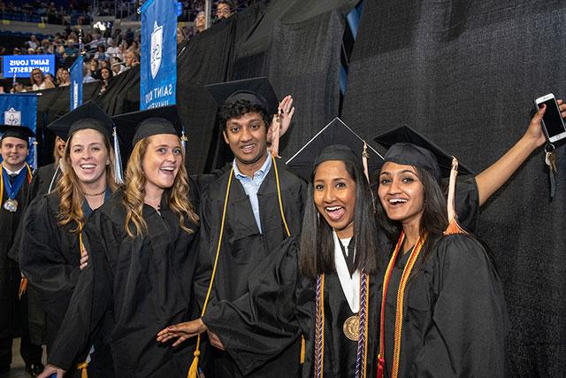 A group of students in graduation caps and gowns pose and smile at the camera