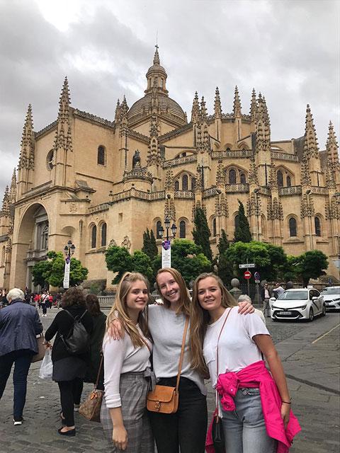 Three students stand with their arms around each other with a castle-type building in the background.