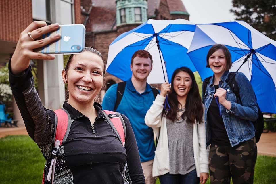 Students taking a selfie under a blue 博彩网址大全 umbrella